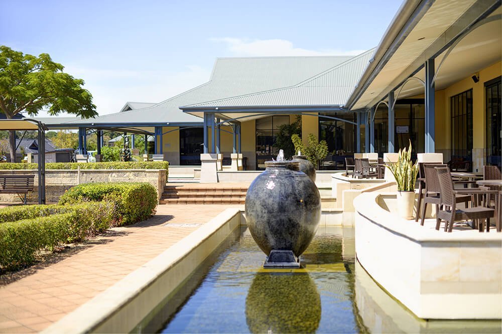 Side exterior view of main Clubhouse at St Ives Murdoch retirement village, featuring pond and garden entry statement