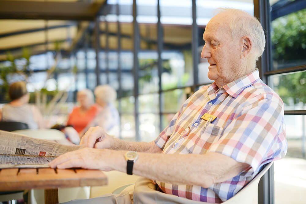 Male retired resident quietly reading the newspaper in the Clubhouse at St Ives Centro retirement village