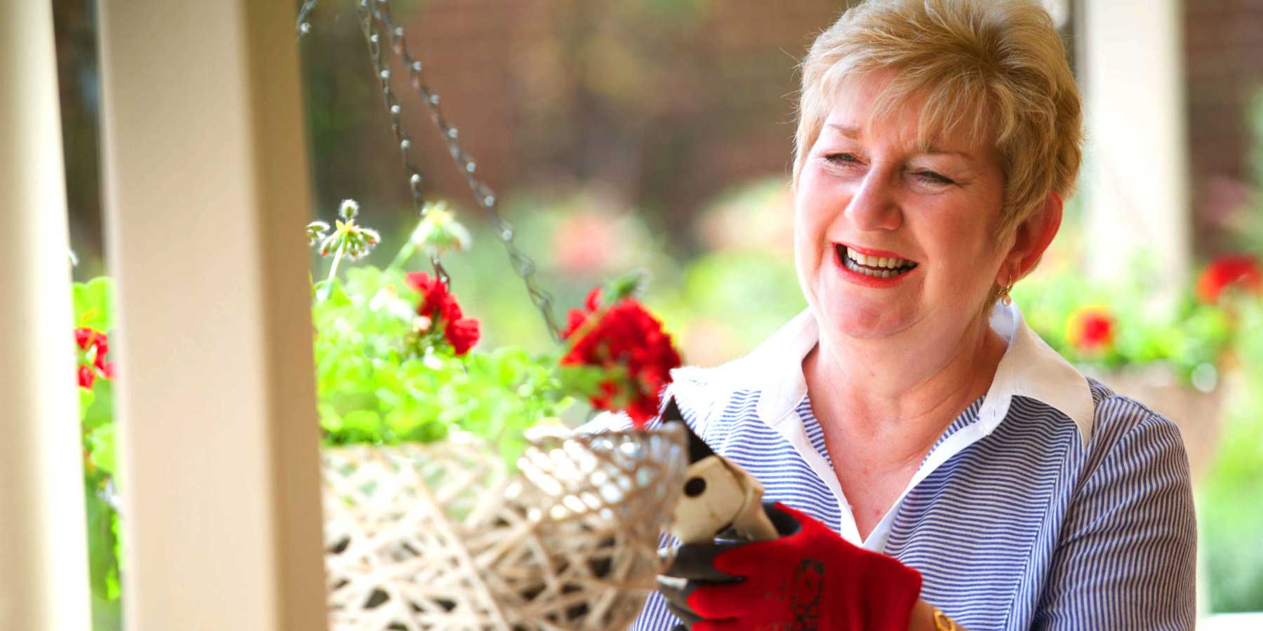 Female resident pruning pot plants outside her home at St Ives retirement village