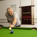 Elderly man smiling as he plays pool